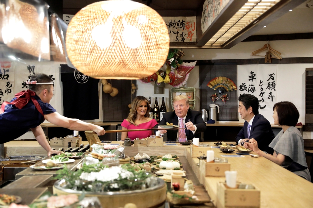 US President Donald Trump, with first lady Melania Trump, receives a plate of food from a chef as they and Japanese Prime Minister Shinzo Abe and his wife Akie Abe have a couples dinner in Tokyo, Sunday. — Reuters