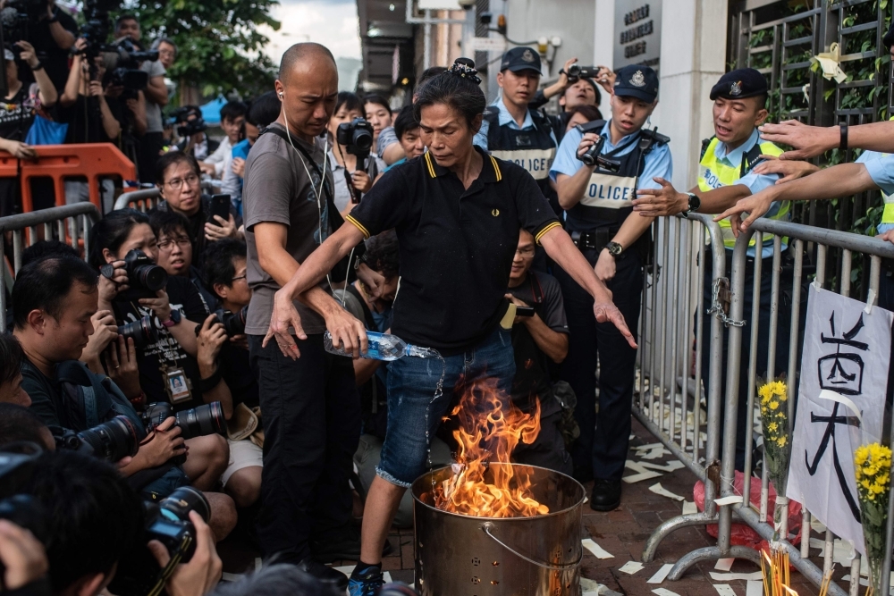 A police officer (left) puts out a fire as pro-democracy activist Lui Yuk-lin burns props outside the Chinese liaison office during a march in Hong Kong Sunday to commemorate the June 4, 1989 Tiananmen Square crackdown in Beijing. — AFP
