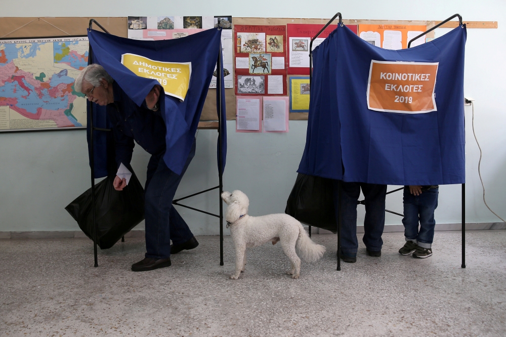 A dog stands next to its owner as he exits the polling booth, during the European Parliament and local elections at a polling station in Athens, Greece, Sunday. — Reuters