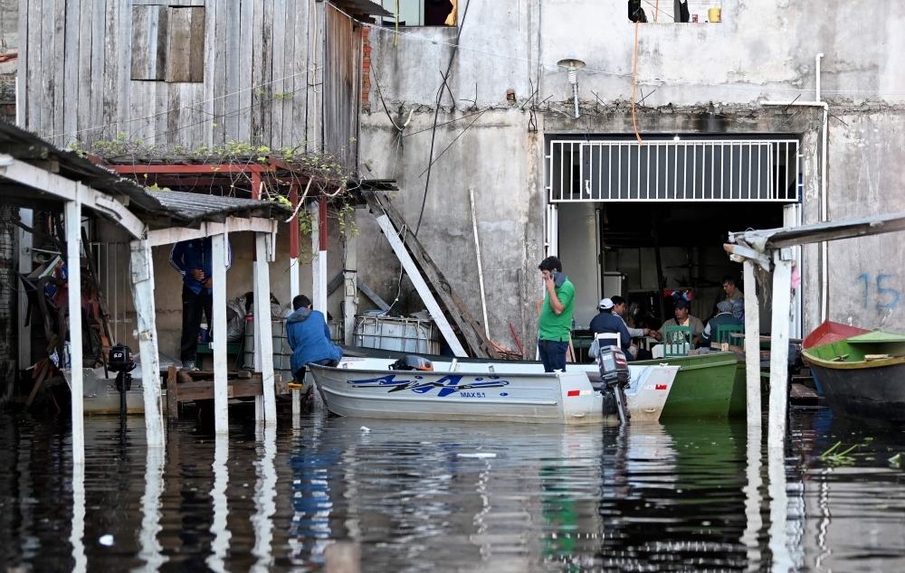 People use a boat to move around the flooded city in Nanawa, Paraguay, on May 25. - AFP  