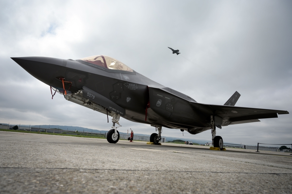 A Lockheed Martin F-35 Lightning II fighter jet is parked on the tarmac at the Payerne Air Base as a Boeing McDonnell Douglas F/A-18 Hornet takes off in the background, during flight and ground tests, as Switzerland is looking for a new fighter jet to replace its aging fleet, on Friday. — AFP