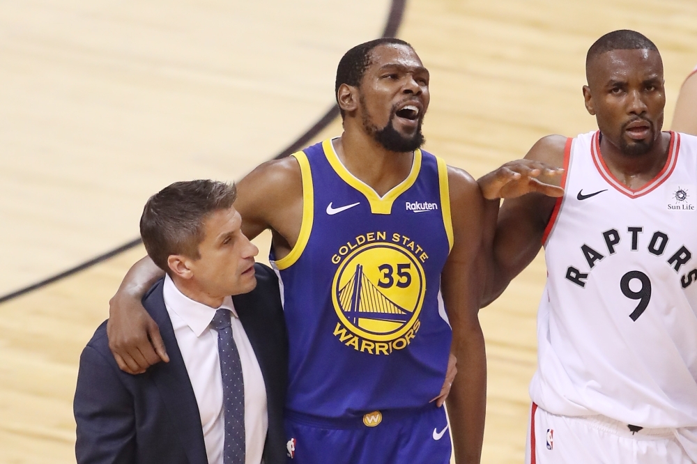 In this file photo Kevin Durant No. 35 of the Golden State Warriors is assisted off the court after sustaining an injury in the first half against the Toronto Raptors during Game Five of the 2019 NBA Finals at Scotiabank Arena.  Durant underwent surgery Wednesday, for a ruptured right Achilles tendon, confirming the injury and the operation in an Instagram posting. — AFP