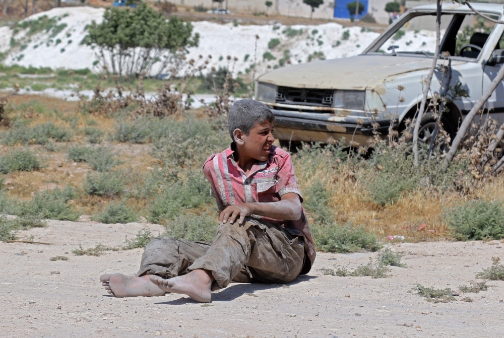 A young Syrian man sits on the ground after a bombing on an industrial area of Idlib, northern Syria, on Monday. — AFP