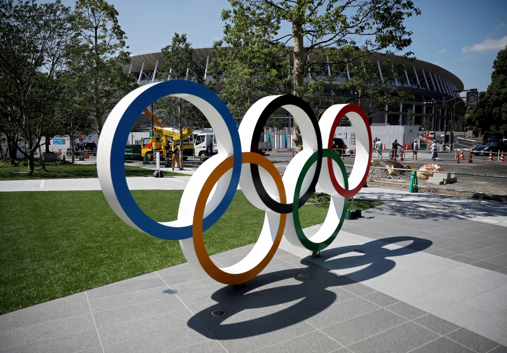 Construction workers and passersby are seen through Olympic rings in front of the construction site of the New National Stadium, the main stadium of Tokyo 2020 Olympics and Paralympics, in Tokyo, Japan in this June 13, 2019, photo. — Reuters