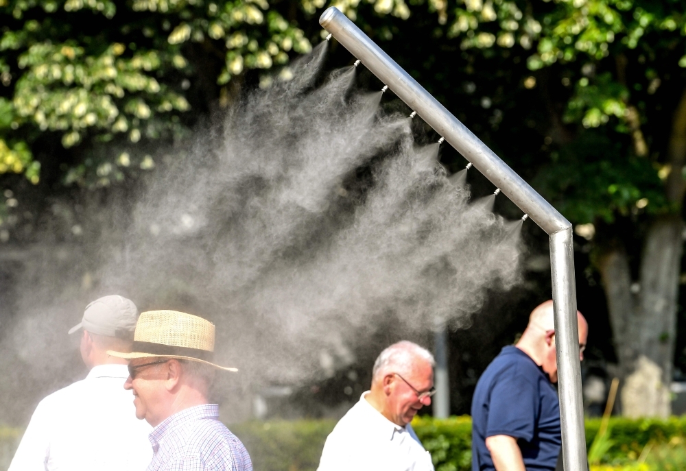 People refresh themselves under a mist sprayer in Lille, northern France, on Wednesday. — AFP