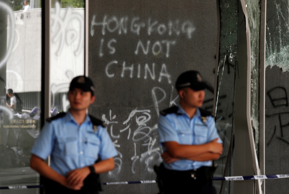 Policemen stand in front of graffiti on the walls of the Legislative Council on Tuesday, a day after protesters broke into the building in Hong Kong. -Reuters