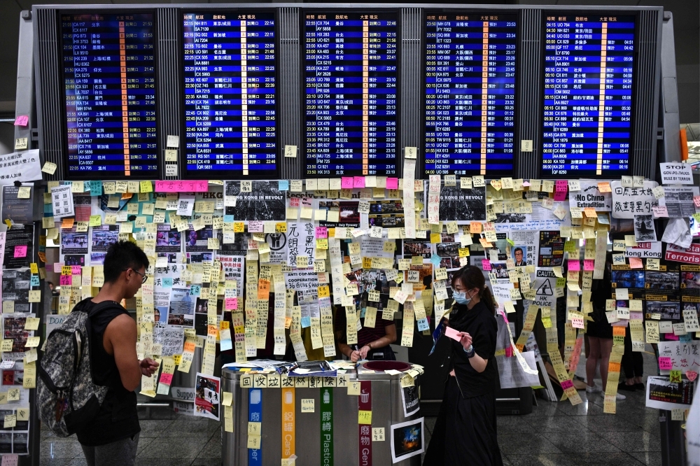 Protesters add notes to a Lennon Wall under a flight display board as they rally against a controversial extradition bill at the arrivals hall of the international airport in Hong Kong on Friday. — AFP