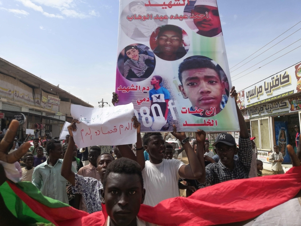 Sudanese protesters march with a poster bearing the portraits of victims, who were shot dead for protesting against a shortage of bread, during a demonstration in the central city of Al-Obeid on Wednesday. — AFP