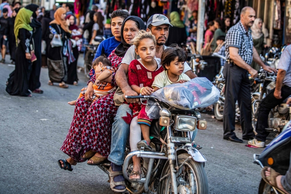 A man rides a motorcycle with a woman and children through a street market in the predominantly-Kurdish northeastern Syrian city of Qamishli in this Aug. 5, 2019 file photo. — AFP