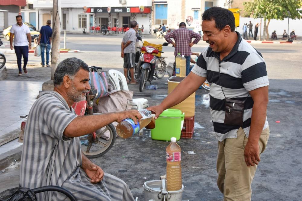 A customer buys a glass of legmi from a street vendor, a coveted date palm drink, in the southwestern Tunisian town of Gabes on July 18. -AFP