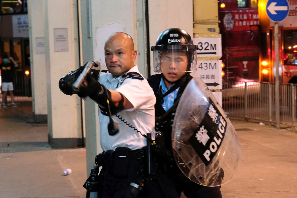 A police officer points a gun at anti-extradition bill protesters who surrounded a police station where detained protesters were being held during clashes in Hong Kong on July 30, 2019. -Reuters