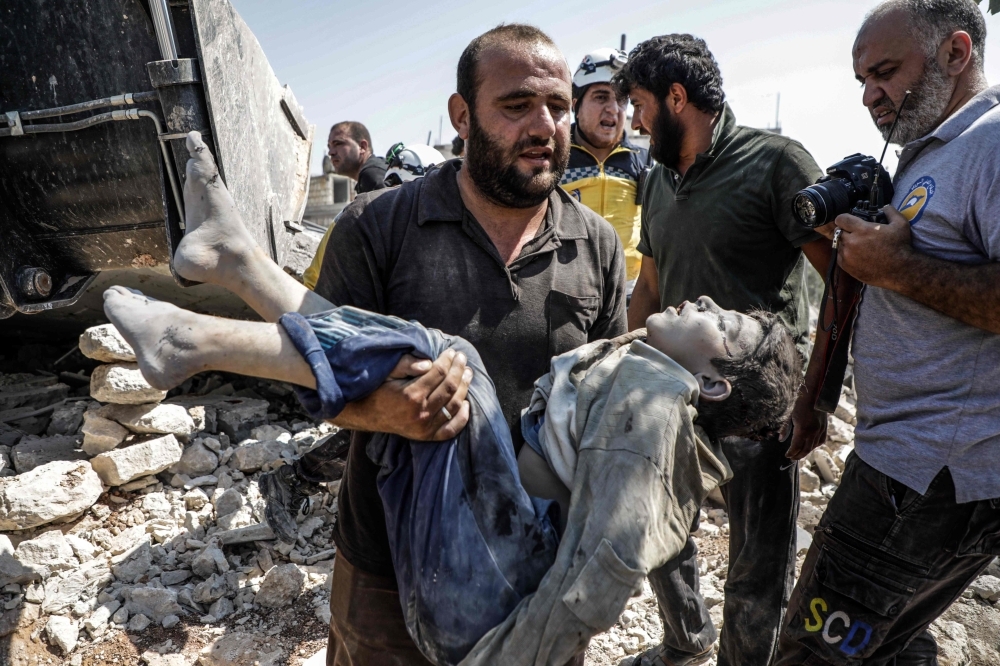 A Syrian carries the body of a child at the site of a reported regime air strike on the village of Deir Sharqi on the eastern outskirts of Maaret al-Numan in Syria's northern province of Idlib on Saturday. -Courtesy photo
