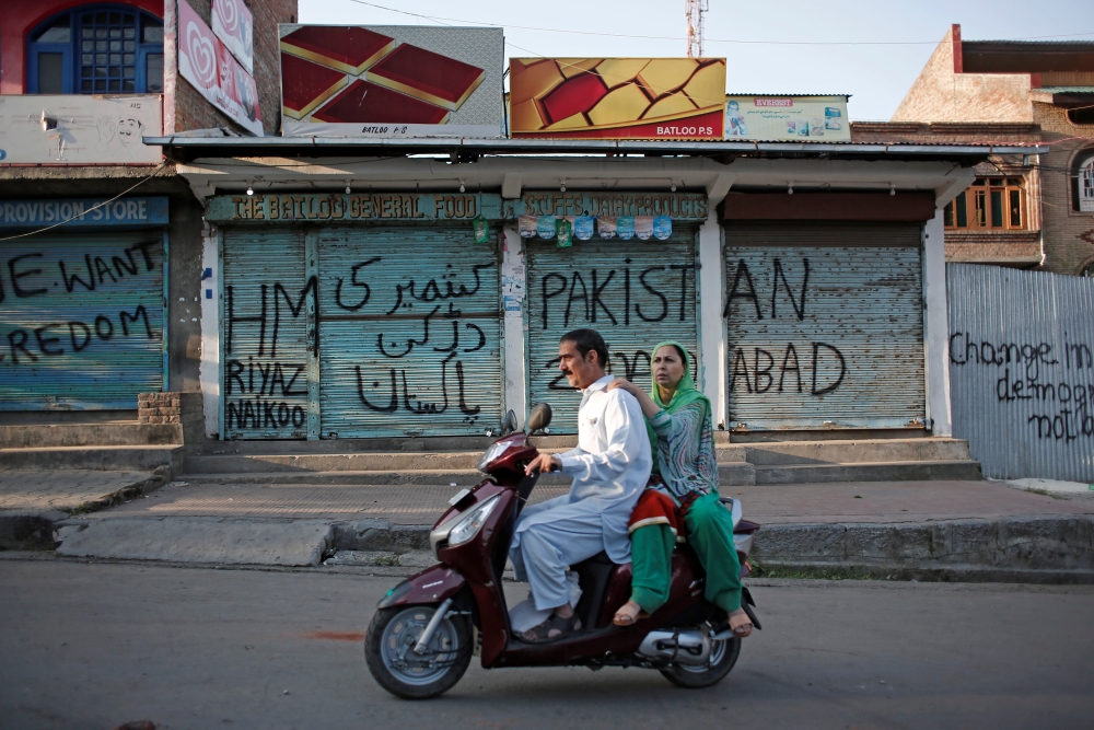 Kashmiris ride on a scooter past the closed shops painted with graffiti during restrictions, after scrapping of the special constitutional status for Kashmir by the Indian government, in Srinagar, India, on Tuesday. — Reuters