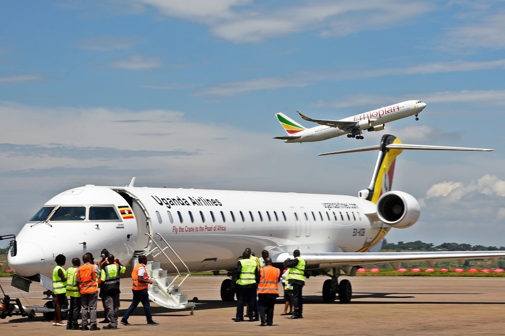 Ground crew prepare a Uganda Airlines Bombadier aircraft for departure as an aircraft operated by Ethiopian airlines takes off in the background at Entebbe airport during the launch of Uganda Airline’s maiden flight to Jomo Kenyatta International Airport in Nairobi, Kenya, on Tuesday. — AFP
