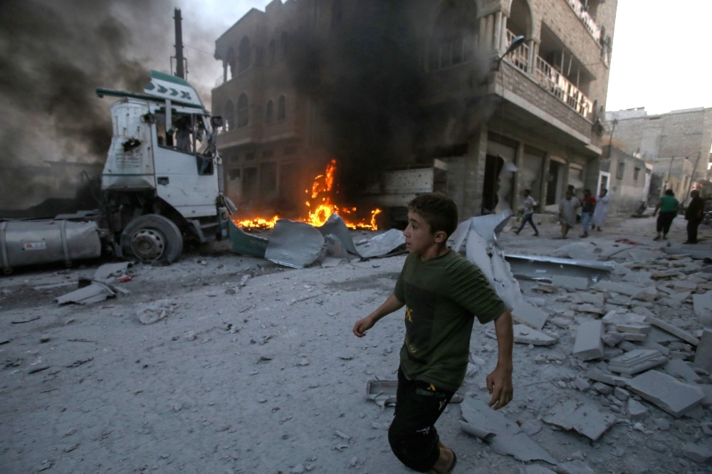 A young boy runs past a fire started in a building following a reported air strike by Syrian regime forces in the area of Maaret Al-Numan in Syria's northwestern Idlib province on Wednesday. — AFP