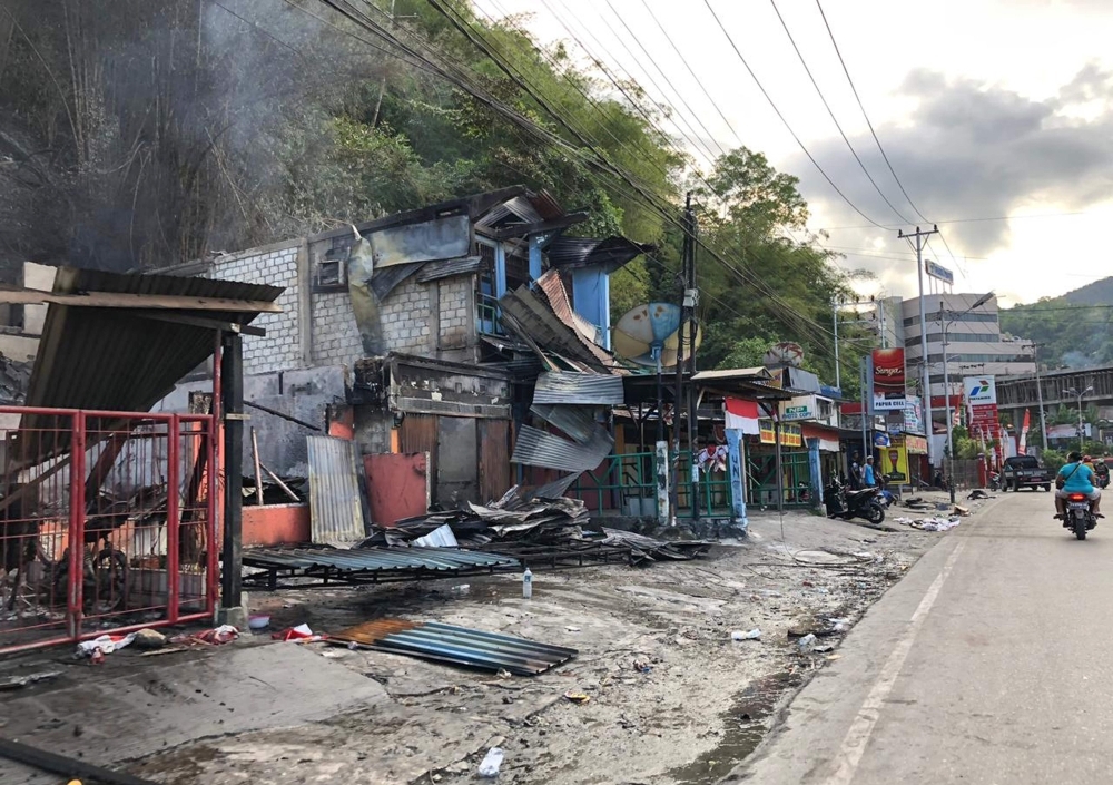 Residents ride motorcycles next to torched shops in Jayapura, Papua, Indonesia, on Friday. — AFP