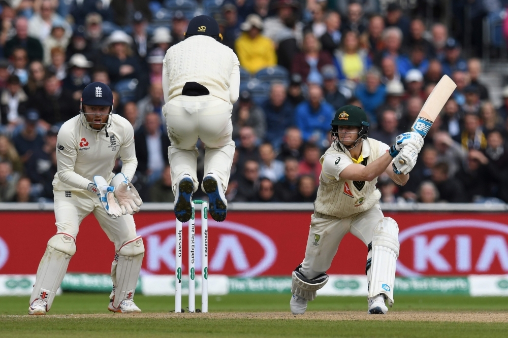 England's Jos Buttler (C) jumps over the ball as Australia's Steve Smith (R), who cracked a double century, hits a shot on the second day of the fourth Ashes cricket Test match at Old Trafford in Manchester, northwest England on Thursday.  — AFP
