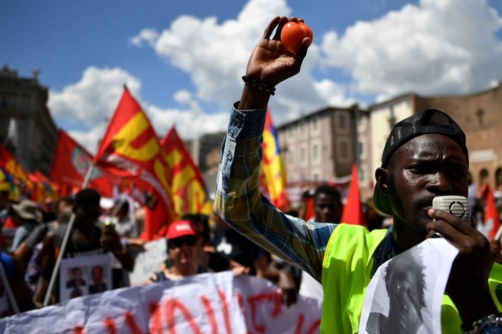 In this file photo taken on June 16, 2018 in Rome, a demonstrator raises a tomato in the air during a march organized by Italy's USB (Base Union of Trade Unions). -AFP