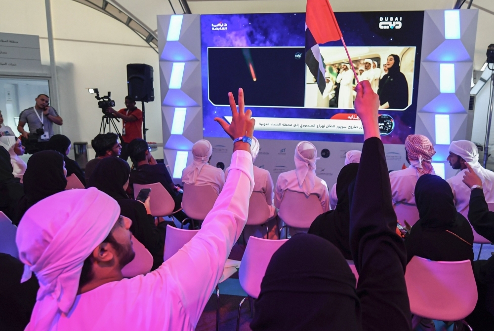 People gesture and wave Emirati national flags as they watch screens showing a Soyuz MS-15 spacecraft lifting off from Baikonur Cosmodrome in Kazakhstan as it carries carrying 35-year-old Emirati astronaut Hazzaa al-Mansoori to spend eight days aboard the International Space Station (ISS), at Mohammed Bin Rashid Space Centre (MBRSC) in Dubai on Wednesday. — AFP