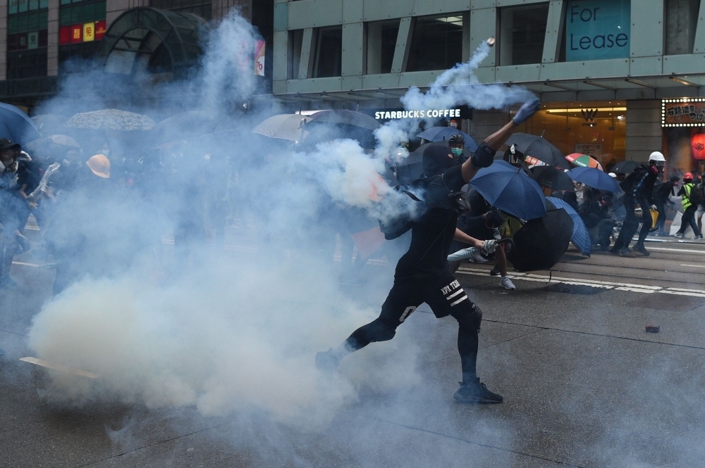 A protester throws back a teargas cannister towards police during a demonstration in the Wanchai district in Hong Kong on Sunday. -AFP 