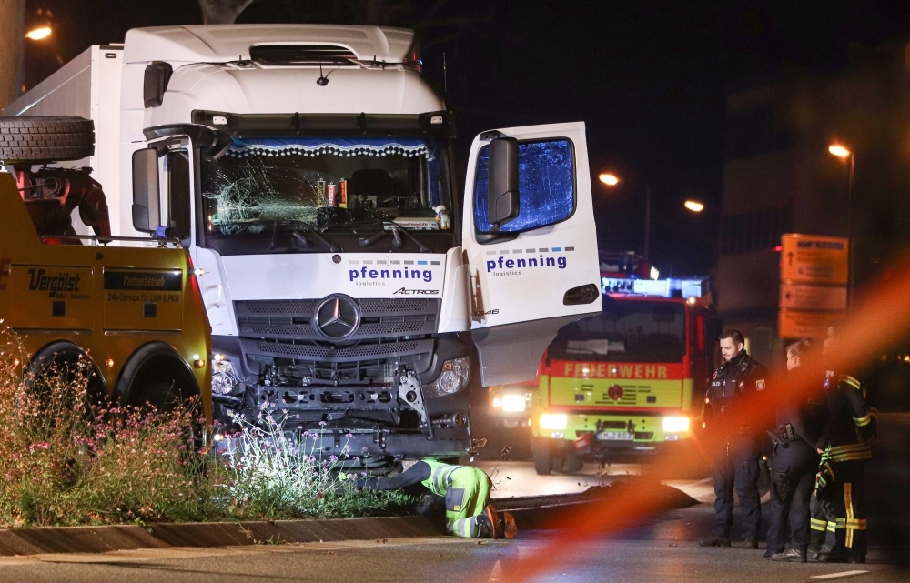 Police officers and firemen look on as a man inspects  on early Tuesday the truck that plowed into several cars late Monday in the center of the German city of Limburg. -AFP