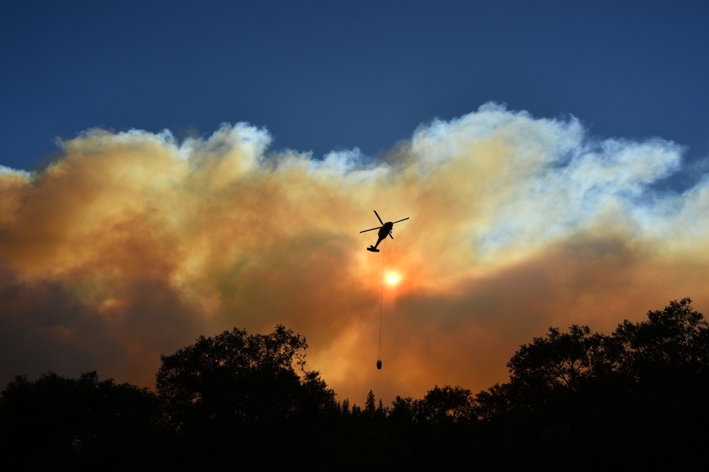 A helicopter passes by the sun as it makes a water drop in the Feather River Canyon, east of Paradise, California, in this Nov. 11, 2018 file photo. — AFP