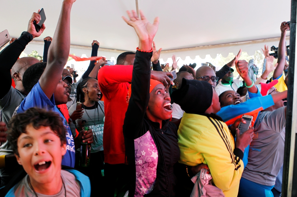 People celebrate as they watch a screen as Eliud Kipchoge, the marathon world record holder, run a marathon in under two hours in Vienna, Austria, at the Karura forest in Nairobi, Kenya, on Saturday. — Reuters
