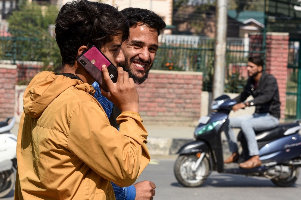 A youth looks on as another one speaks on a mobile phone in Srinagar on Monday, following Indian government's decision to restore mobile phones network in Indian-administered Kashmir. — AFP