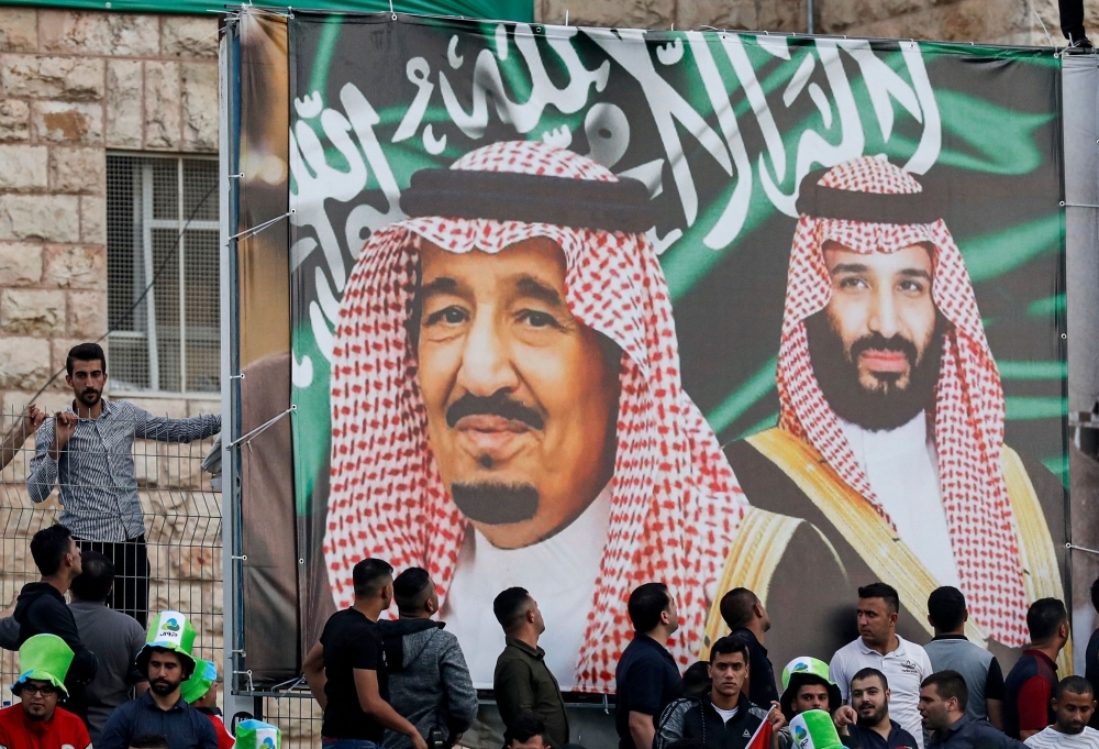 Football fans stand beneath a large banner depicting Saudi Arabia's King Salman (C) and his son Crown Prince Mohammed bin Salman (R) as they attend the World Cup 2022 Asian qualifying match between Palestine and Saudi Arabia in the town of Al-Ram, West Bank, on Tuesday. — AFP