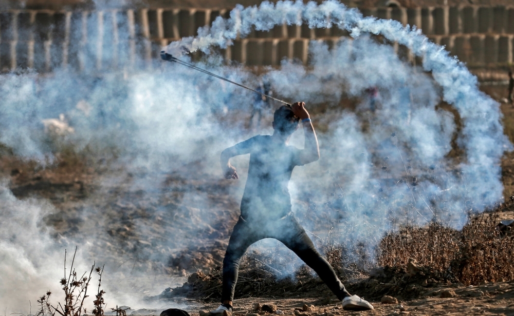 A Palestinian protester uses a slingshot to throw back a tear gas canister at Israeli forces amidst clashes during a demonstration along the border with Israel east of Bureij in the central Gaza Strip on Friday. — AFP