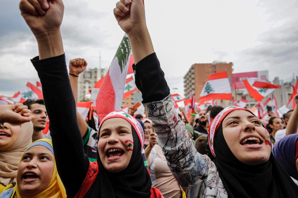  Women wearing bandanas showing the Lebanese national flag chant slogans during a demonstration in the northern city of Tripoli's Al-Nour Square on Wednesday, on the seventh day of protest against tax increases and official corruption. — AFP