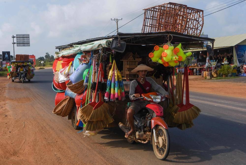 Cambodian vendors ride their motorcycle carts loaded with various household merchandise for sale along a road in Kampong Cham province.  — AFP 