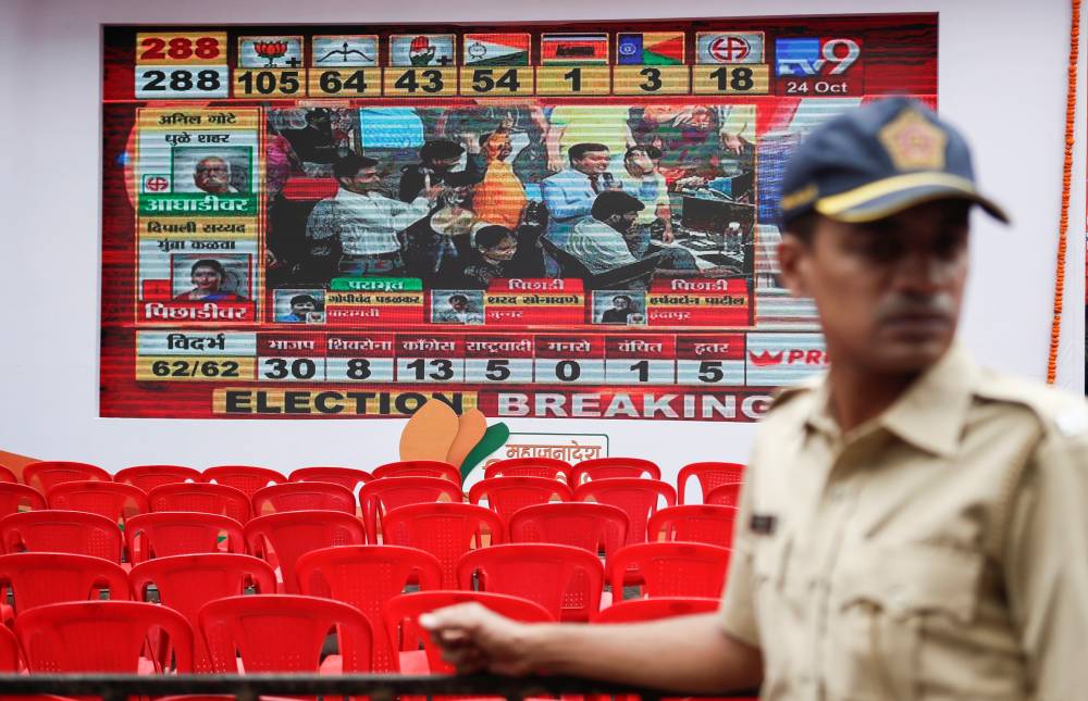 A policeman stands in front of a screen displaying Maharashtra state election results in Mumbai, India, Thursday. — Reuters