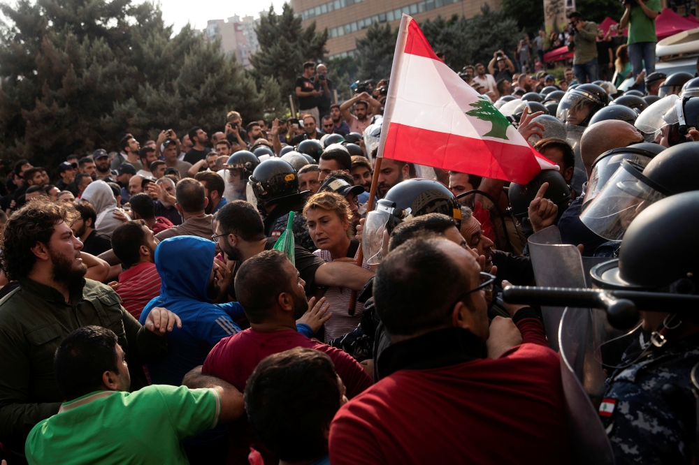 A woman holds a Lebanese flag as riot police confront Hezbollah supporters during ongoing anti-government protests in downtown Beirut, Lebanon, on Friday. — Reuters