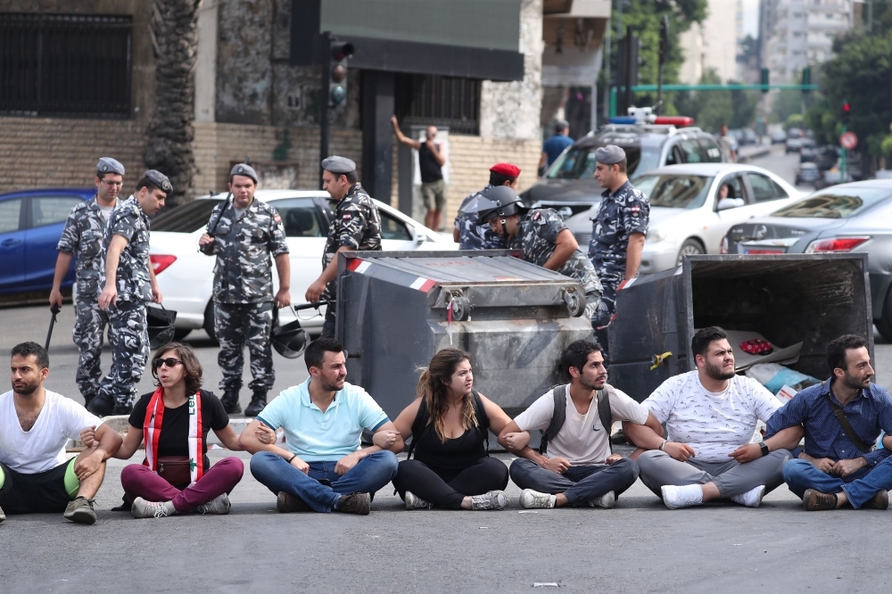 Lebanese protesters sit on the ground to block a major bridge in the center of the capital Beirut during an anti-government demonstration on Saturday. Demonstrators across Lebanon blocked roads and took to the streets today for a 10th consecutive day, defying what they said were attempts by Hezbollah to defuse their movement and despite tensions with the army. — AFP