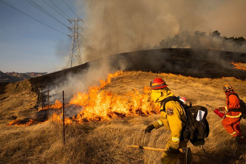 A back fire set by fire fighters burns a hillside near PG&E power lines during firefighting operations to battle the Kincade Fire in Healdsburg, California on Saturday. — AFP