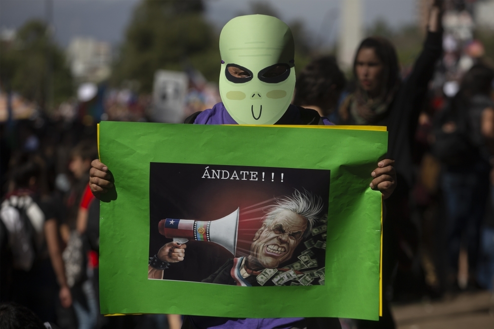 A masked man holds a sign with a caricature depicting Chilean President Sebastian Pinera reading 