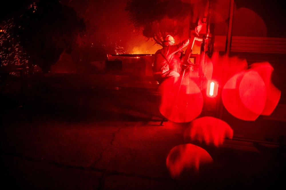 A firefighter climbs his firetruck as wind-whipped flames and embers light multiple homes on fire during the Hillside fire in the North Park neighborhood of San Bernardino, California, on Thursday. — AFP