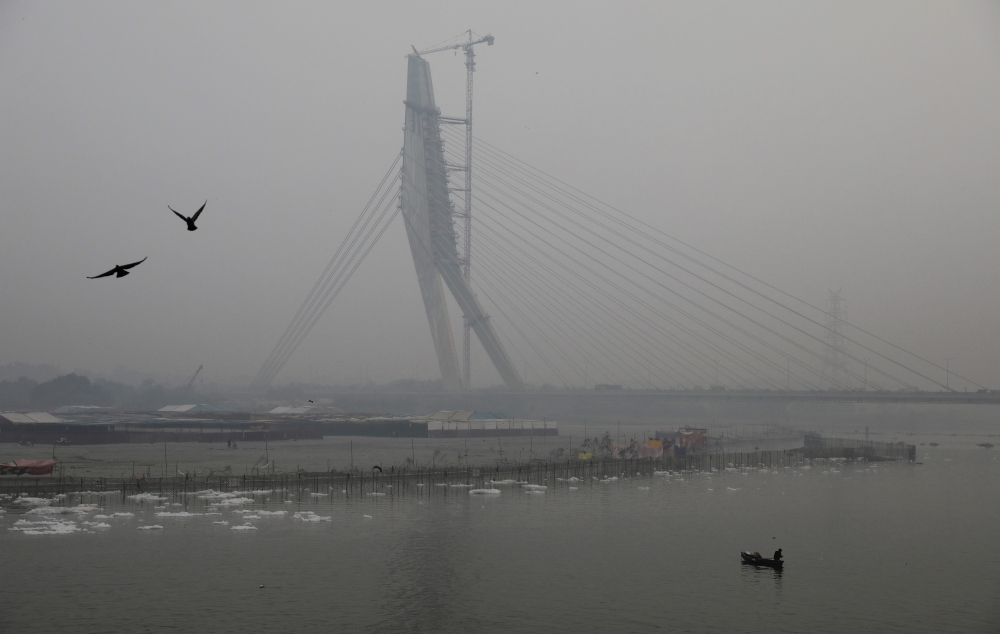 A man paddles a boat in the waters of the Yamuna river near the Signature bridge on a smoggy evening in New Delhi, India, on Friday. — Reuters