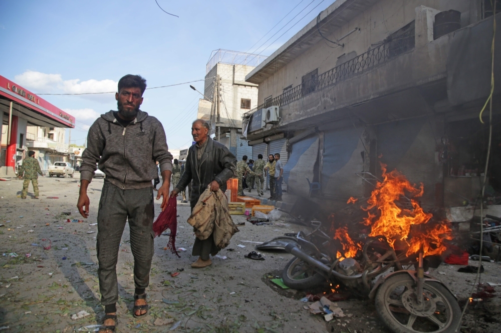 Syrians walk past a burning motorcycle at the site of a car bomb explosion in the northern Syrian Kurdish town of Tal Abyad, on the border with Turkey, on Saturday. — AFP