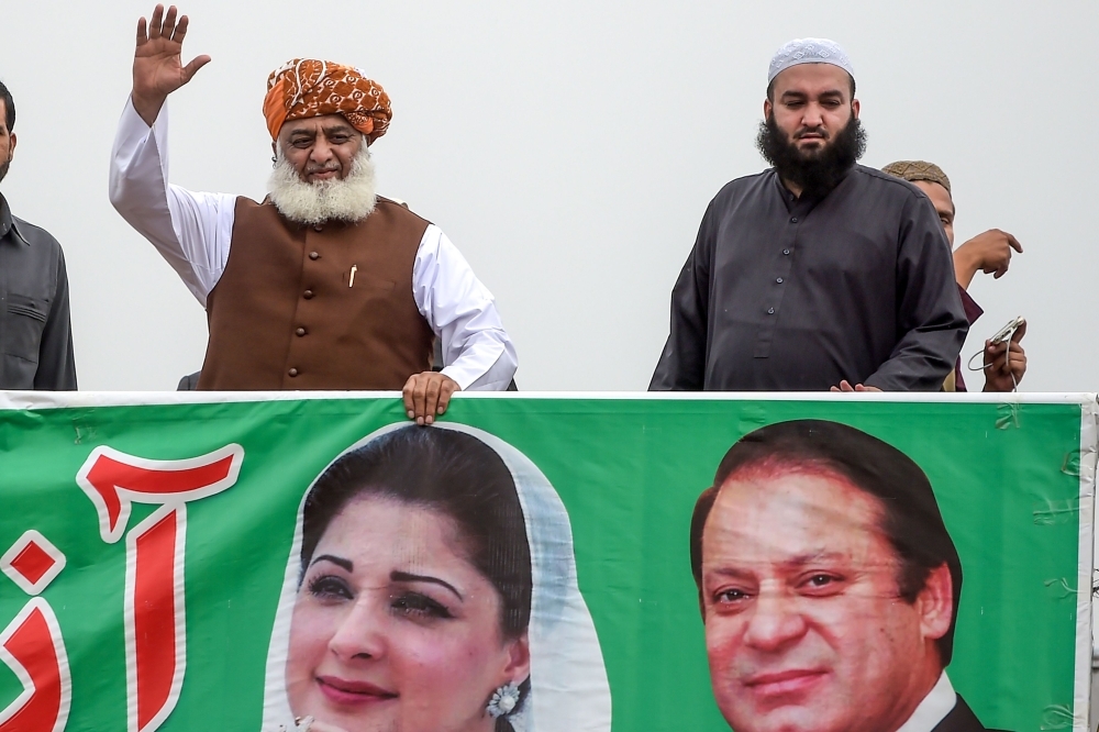 Islamic political party Jamiat Ulema-e-Islam (JUI-F) leader Maulana Fazlur Rehman, left, waves as he holds a banner showing photographs of jailed former Pakistan's Prime Minister Nawaz Sharif, right, and his daughter Maryam Nawaz during an anti-government 