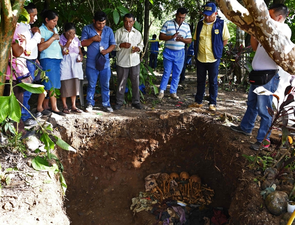 People pray around human remains -allegedly belonging to their relatives- during their exhumation by a team of international forensics at the Yancolo hamlet, in Cacaopera, El Salvador, on Wednesday. — AFP