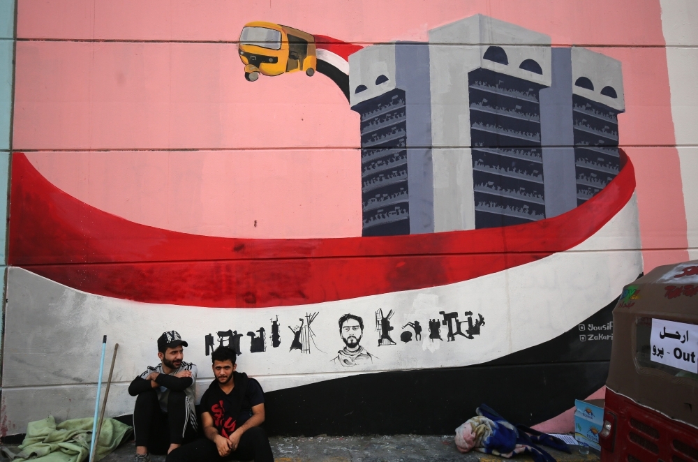 Iraqi protesters rest in front of a mural in Baghdad's Tahrir Square on Friday as the Iraqi capital braces for another day of anti-government demonstrations. -AFP