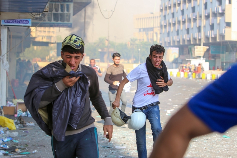 Iraqi protesters run for cover from teargas fired by security forces in Al-Khalani square in central Baghdad on Sunday. -AFP