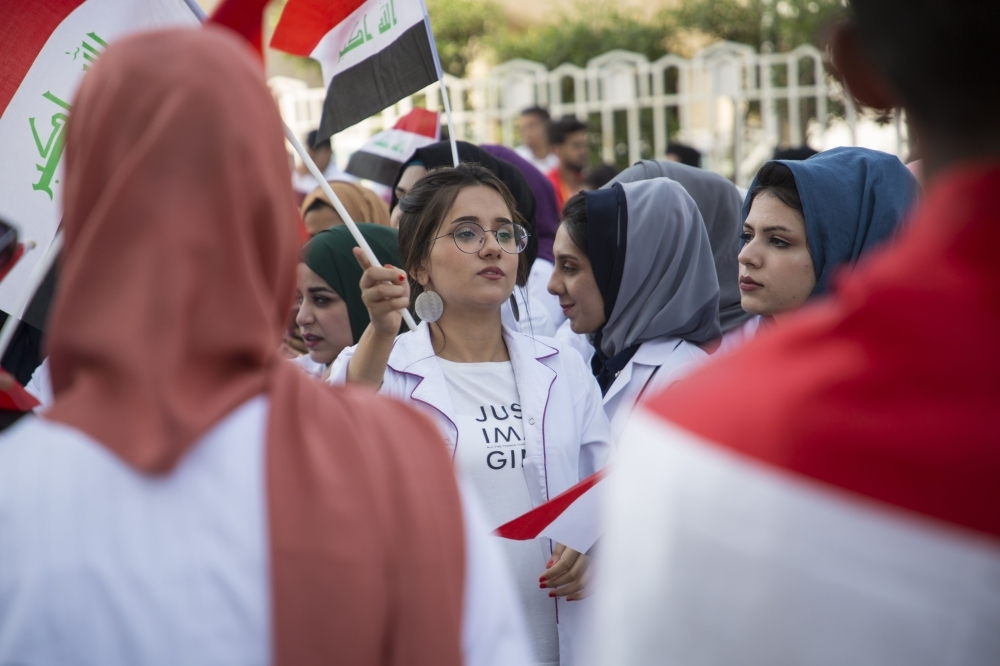 Iraqi medical students wave the national flag as they take part in ongoing anti-government protests at their campus in the southern city of Basra, on Sunday. Iraqi protesters struggled to keep up their anti-government sit-ins following a deadly crackdown by security forces. — AFP