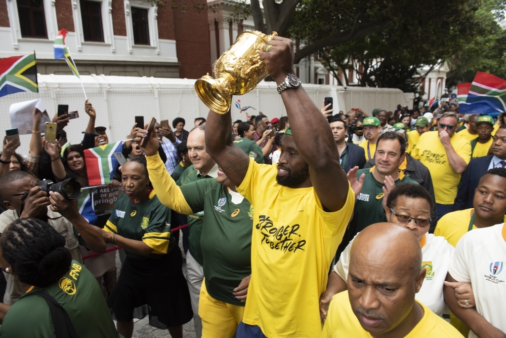 South African Rugby scrumhalf Faf de Klerk (C)  holds the Web Ellis Trophy, while the rest of the Springboks team stands beside him, during the South African Rugby World Cup winner team's last stop to parade the Web Ellis Trophy at the South African Parliment  in Cape Town on Monday. — AFP