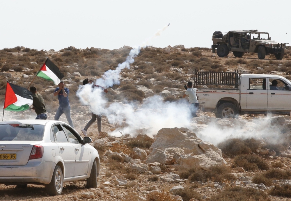Palestinian demonstrators throw a teargas canister back at Israeli soldiers during a demonstration against the confiscation of land in the village of Al-Shayukh, east of the West Bank city of Hebron, on Sunday. — AFP