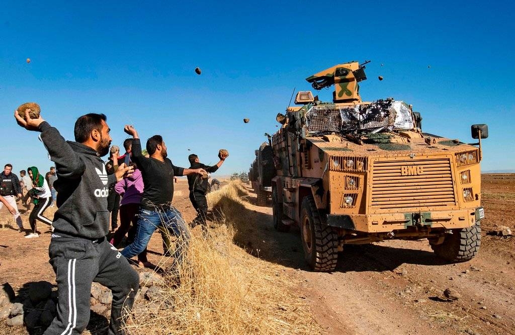 Kurdish demonstrators throwing rocks at a Turkish military vehicle on Friday during a joint Turkish-Russian patrol near the town of Al Muabbadah in northeastern Syria. (AFP)