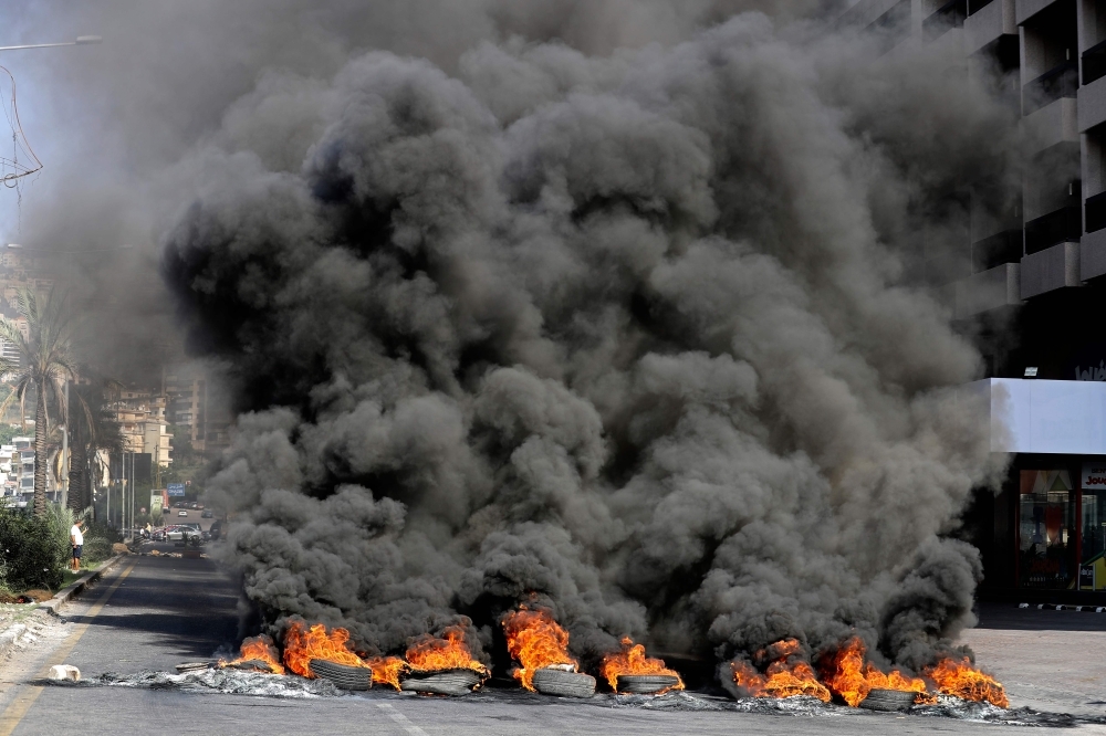 A Lebanese youth waves a national flag in front of burning tires blocking the Beirut-Tripoli highway in the coastal town of Ghazir, north of the port city of Junieh, during continuing anti-government protests across Lebanon on Wednesday. -AFP