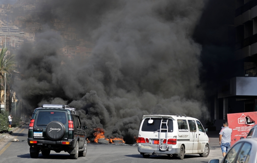 A Lebanese youth waves a national flag in front of burning tires blocking the Beirut-Tripoli highway in the coastal town of Ghazir, north of the port city of Junieh, during continuing anti-government protests across Lebanon on Wednesday. -AFP